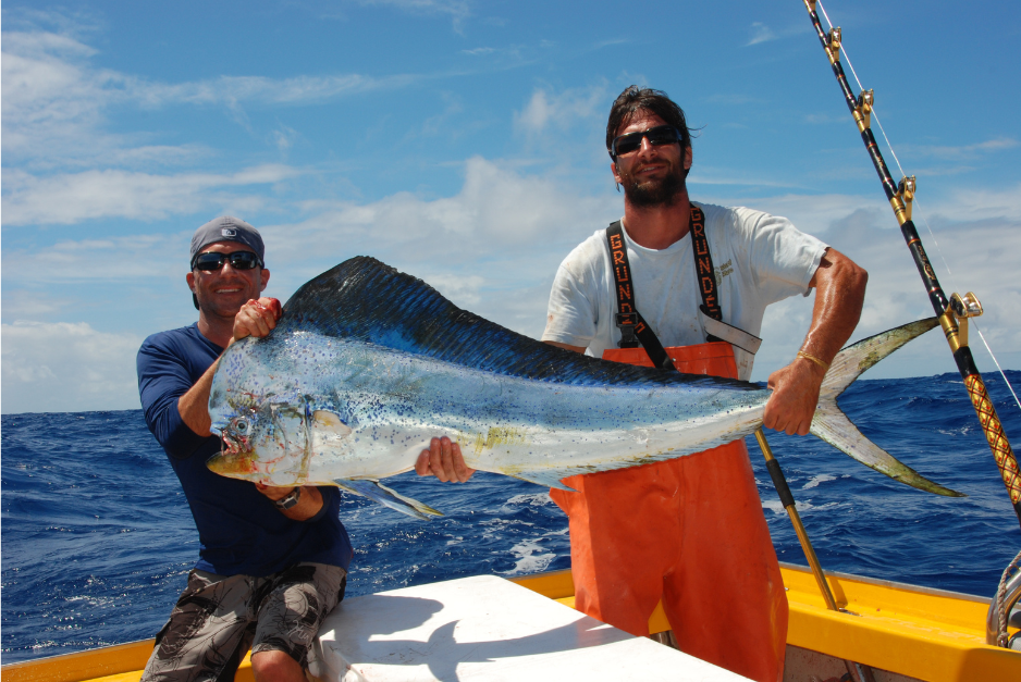 Two scientists holding a large mahi mahi fish while out at sea.